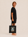Model carrying the Permanent Vacation cotton tote bag by Mojo Circus